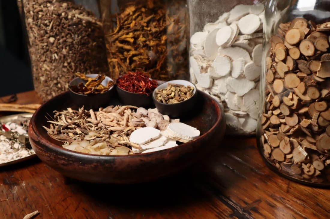 Dried medicinal roots and bark in bowls and jars on a dark table