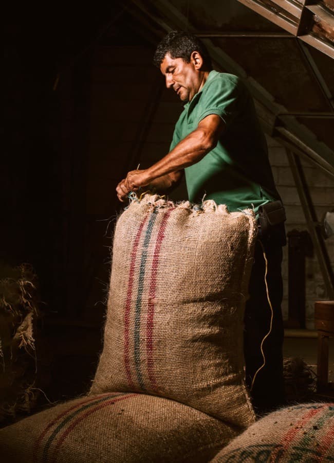 A worker hand-stitching a filled sack closed in an export warehouse