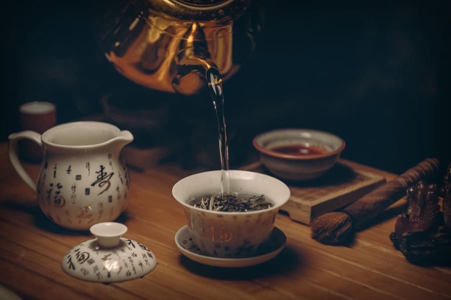 A brass kettle pouring hot water over loose leaf tea
