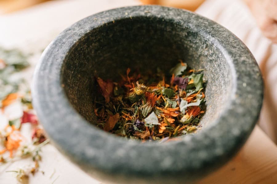 A granite mortar filled with mixed dried herbs and petals